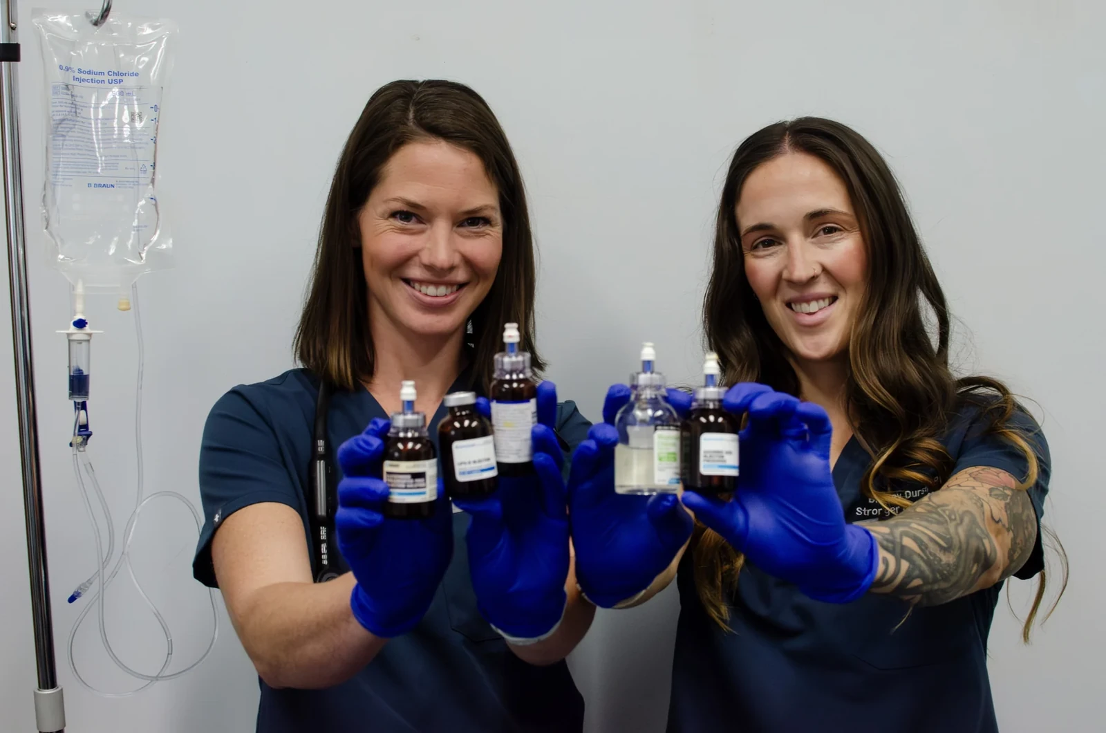 Two gloved clinicians holding labeled vials beside a saline bag and tubing